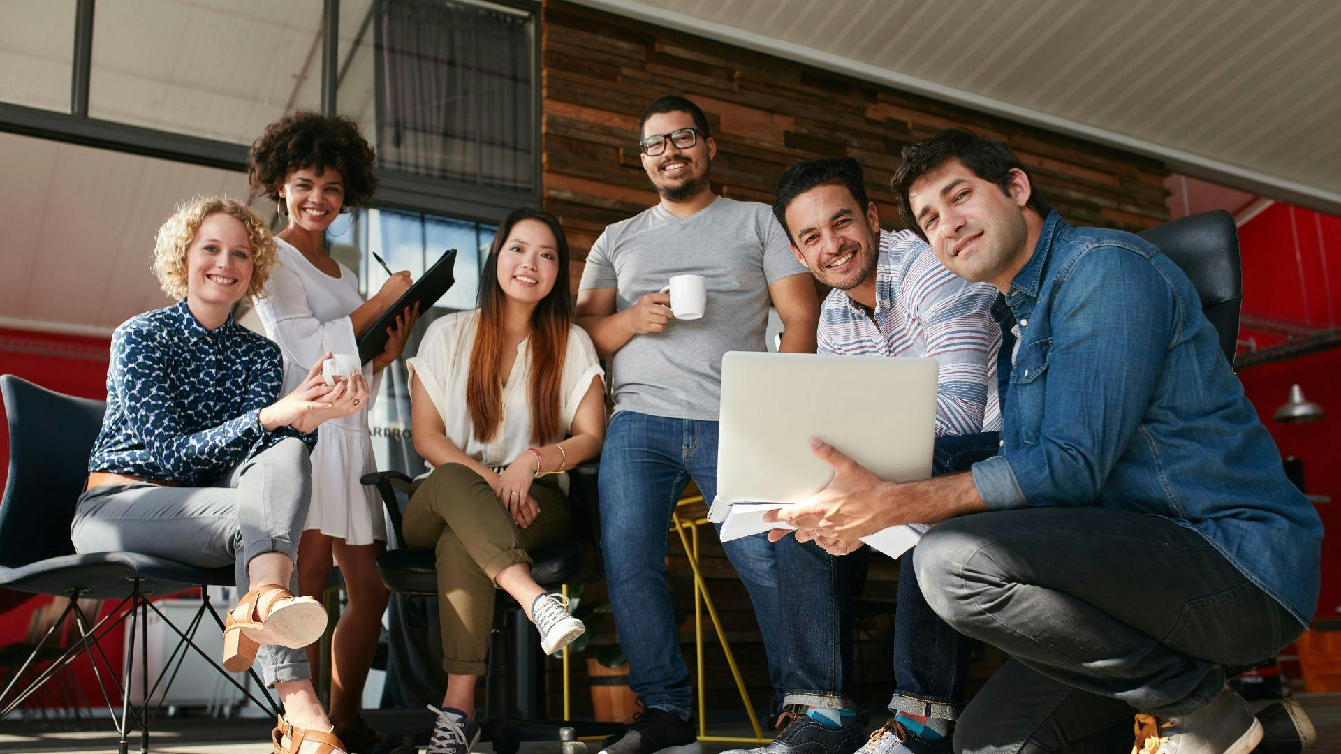 A cheerful group of individuals sitting on chairs at work, wearing smiles on their faces.