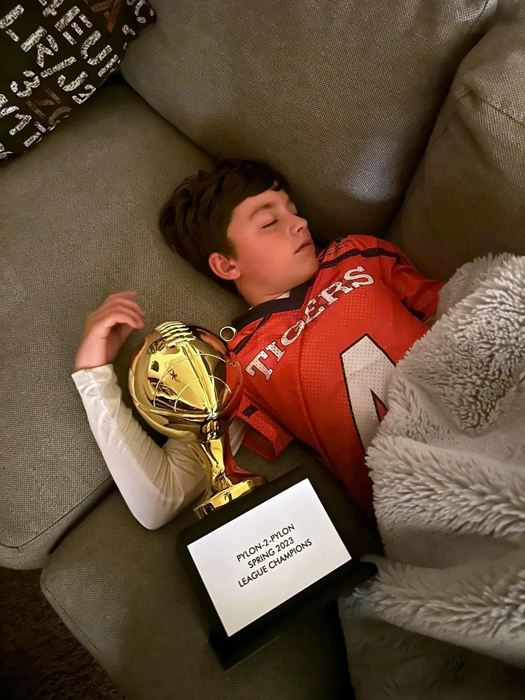 A flag football kid sleeping with his trophy