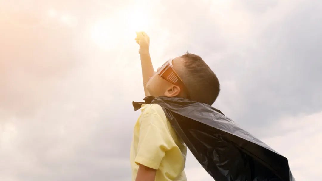 A child wearing sunglasses and a cape holding up the sun