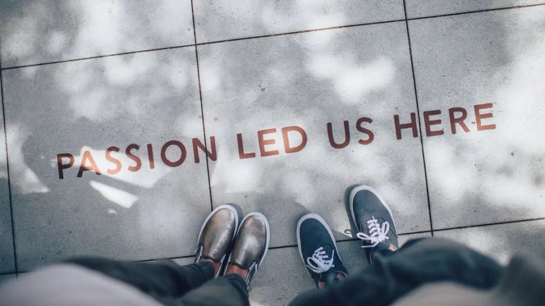 A person's feet and shoes on a tile floor that reads "passion led us here"