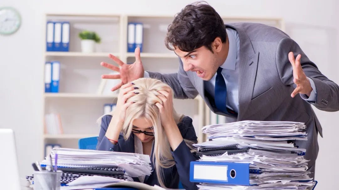 Male colleague screaming at female colleague as she holds her head in her hands