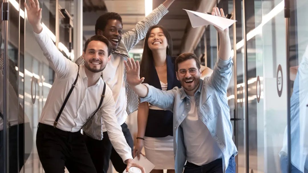 Four happy colleagues with hands up in the air