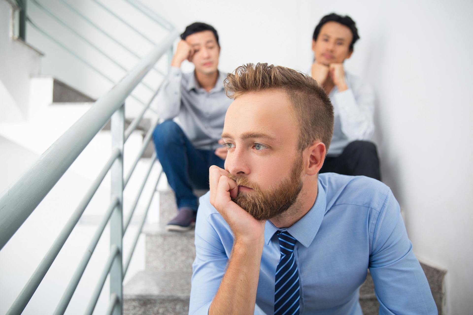 3 colleagues sitting on stairs, distracted and low