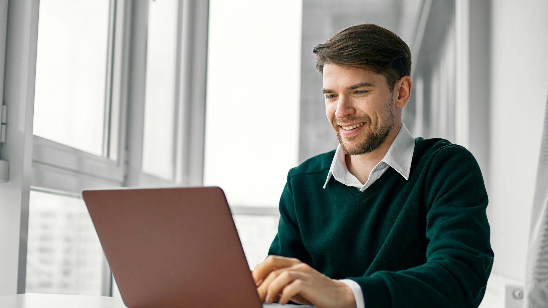 A man smiling while using a laptop to work or browse the internet.