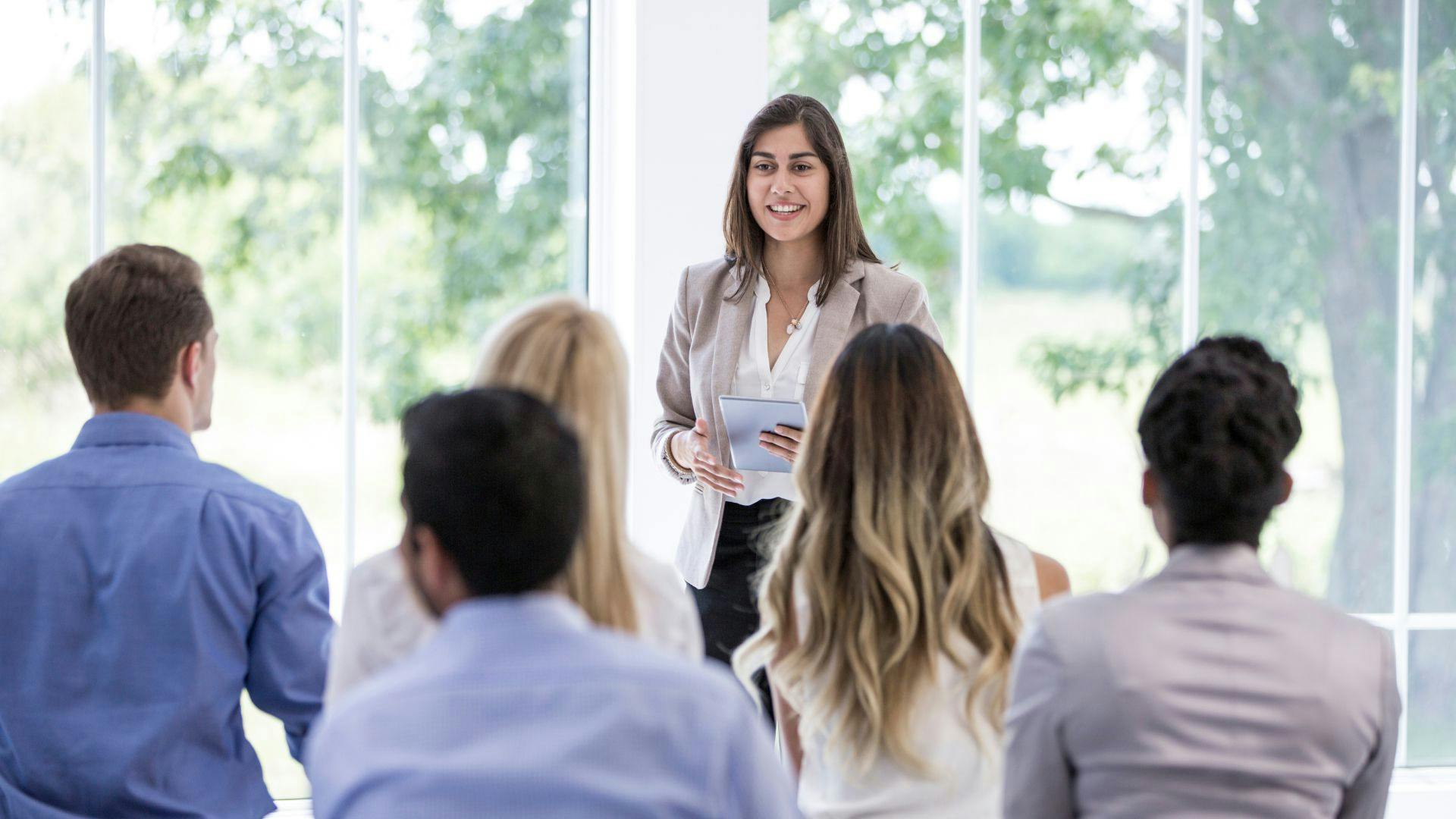 A woman confidently presenting to a group of attentive individuals during a professional meeting.