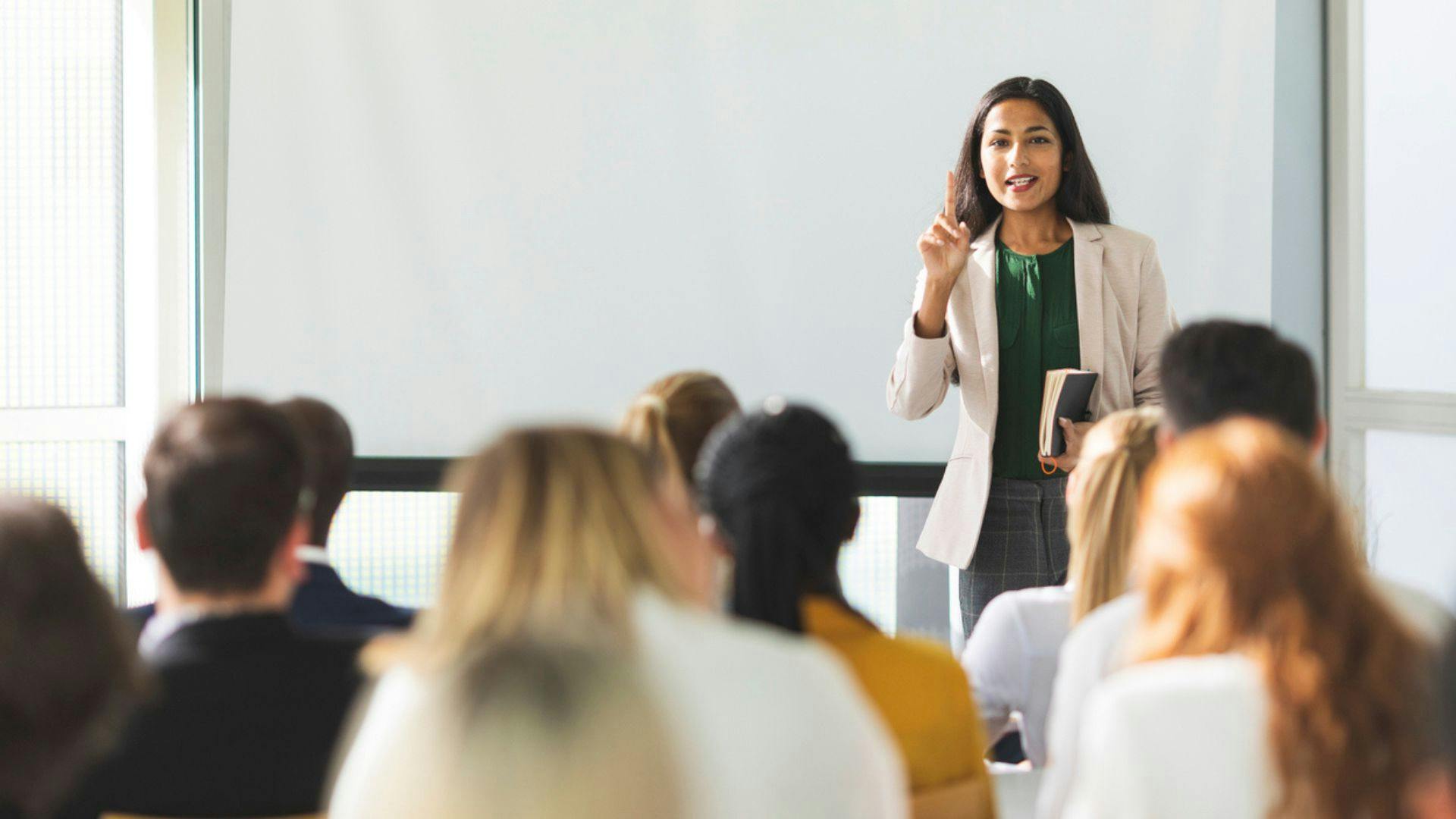 A woman confidently presenting to a diverse audience in a conference room.