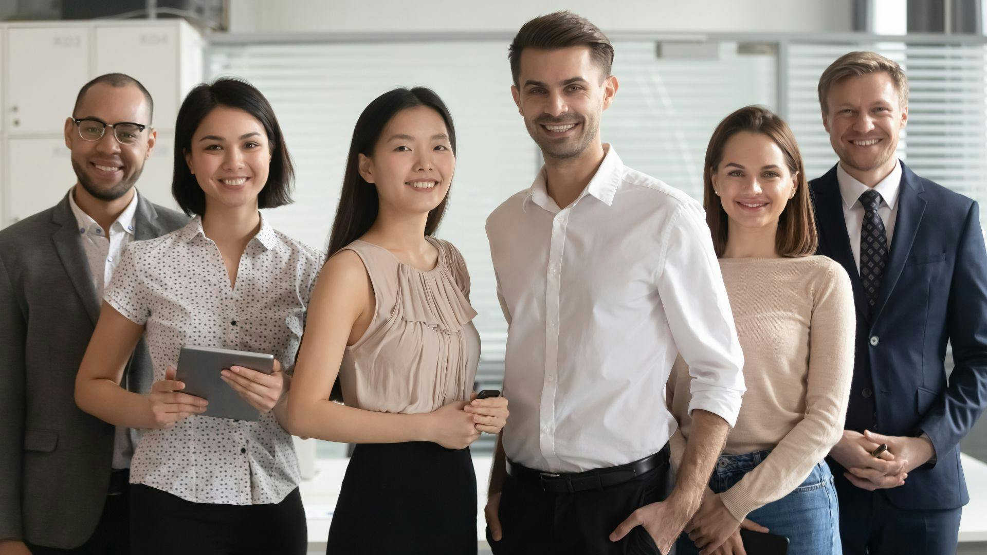 A diverse group of professionals in business attire standing together in a modern office setting.