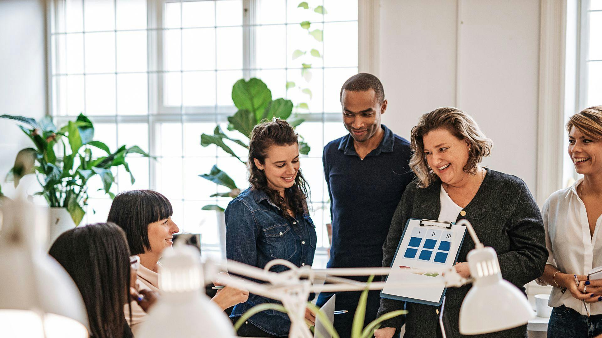 A group of coworkers in a meeting gathered around a table reviewing a report together. 