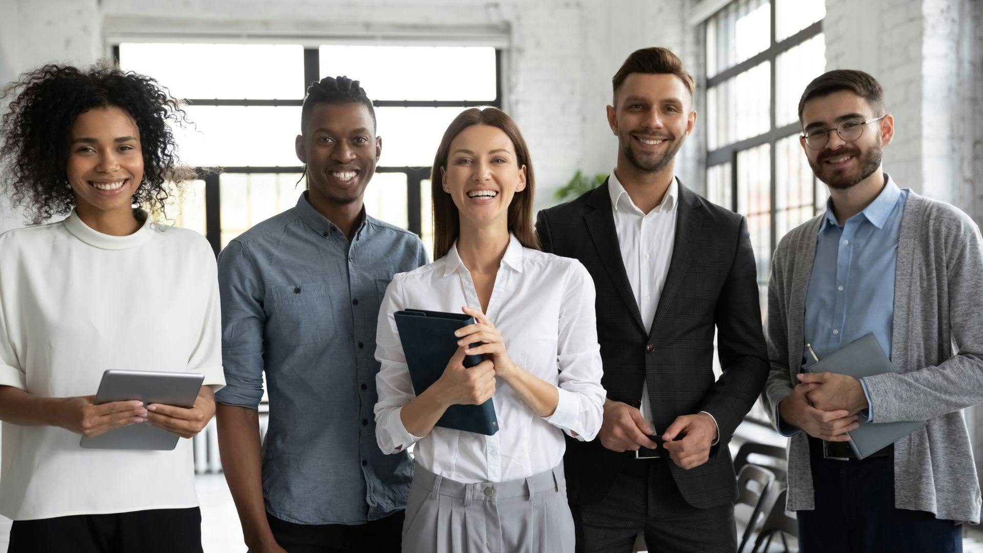 Five office employees in a workplace setting looking at the camera and smiling. 