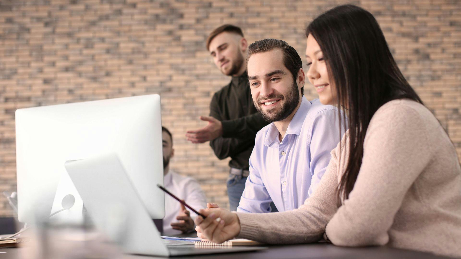 A team of professionals sitting around a computer, working together on a project or presentation.