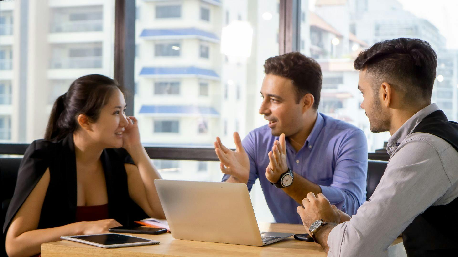 Group of three people gathered around a laptop on a table.