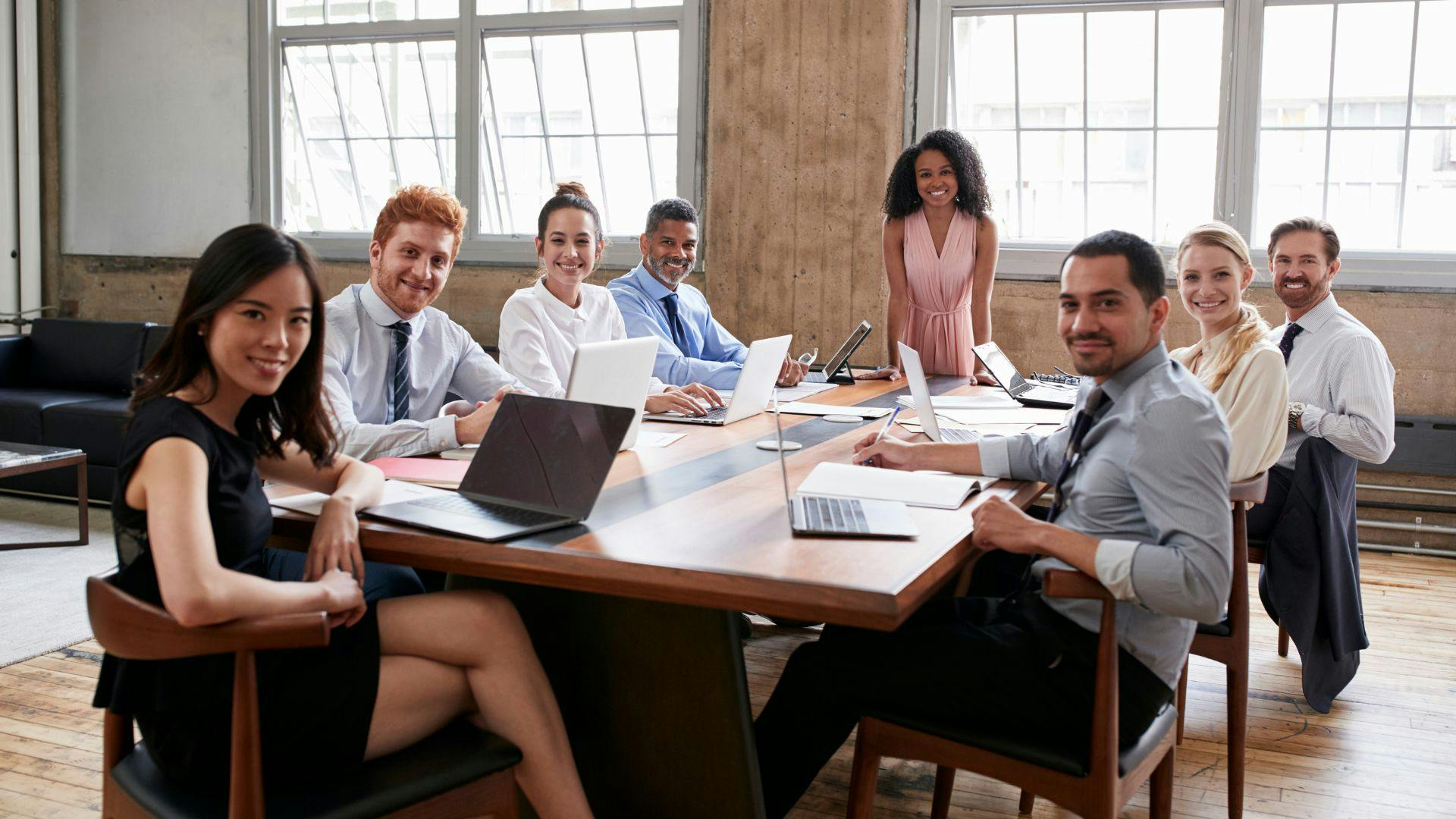 A team of coworkers sitting together at a table, likely brainstorming or working on a project, turned looking at the camera and smiling.