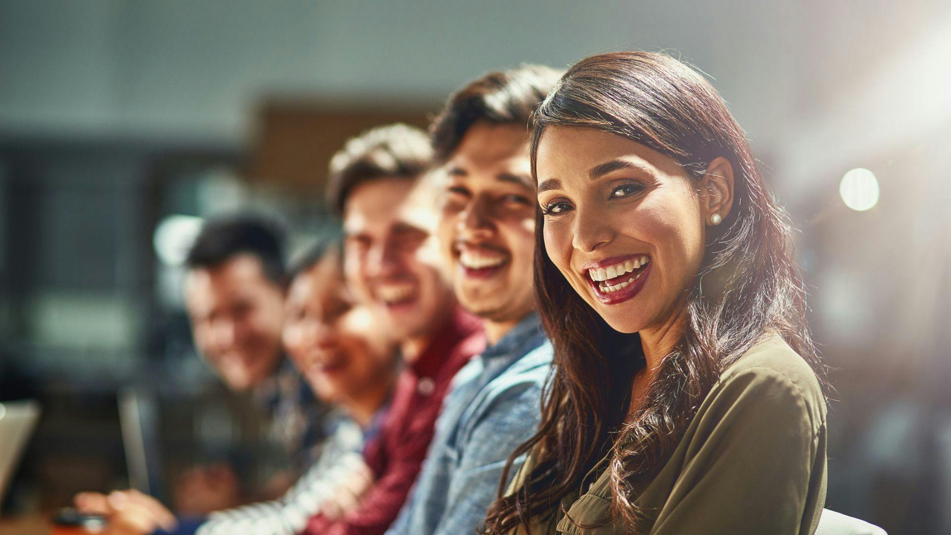 A happy group of coworkers sitting together at a table, looking at the camera and smiling.