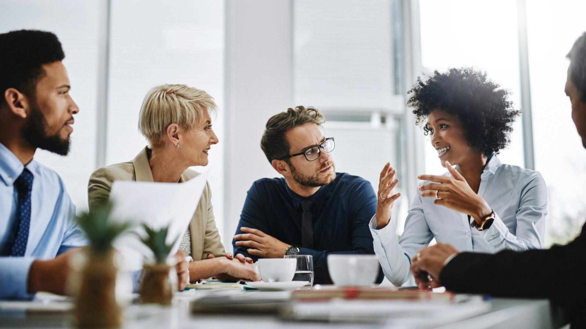 A group of business professionals engaged in a meeting around a conference table in a modern office setting.